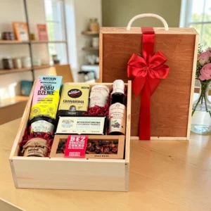 Zdrowy zestaw upominkowy w drewnianej skrzynce z ciemnym wieczkiem i czerwoną kokardą. Wewnątrz znajdują się: kawa Caffè Vergnano Granaroma, herbata Natjun Nuwara Eliya, sok porzeczkowy, miód wielokwiatowy, dżem z borówki oraz rzemieślnicza czekolada z owocami bez cukru na czerwonym wypełnieniu.