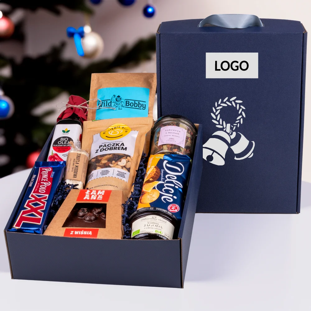 Granatowe pudełko prezentowe z rączką, ustawione na drewnianym stoliku obok filiżanki kawy. Zestaw zawiera polskie produkty: Prince Polo, Delicje, rzemieślniczą czekoladę z wiśnią, konfiturę jagodową oraz herbatę liściastą. Stylowy prezent okolicznościowy z polskimi akcentami.